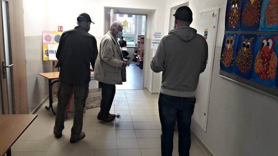 Voliči čekají na chodbě, než budou moct, v omezeném počtu vstoupit do volební místnosti